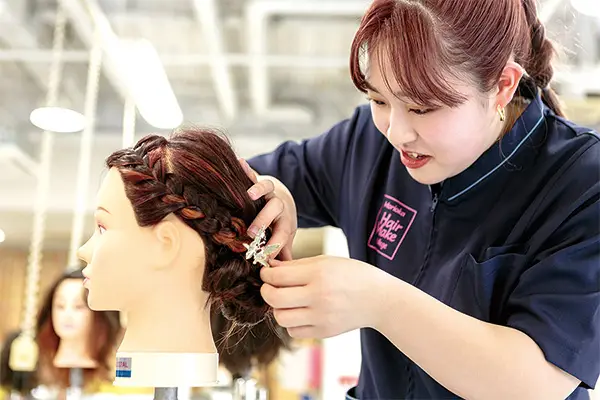 マネキンで編み込みのヘアアレンジ練習をする学生