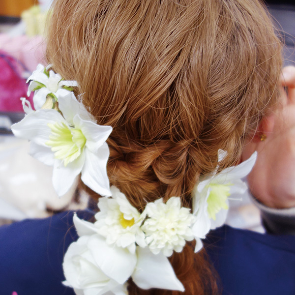 編み込みされた髪型。白い花のヘアアクセサリーでまとめている。
